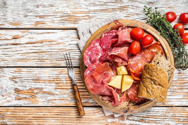 Prato de carnes frias, tapas tradicionais espanholas de charcutaria em uma placa de madeira. Fundo de madeira branco. Vista do topo. Copie o espaço.