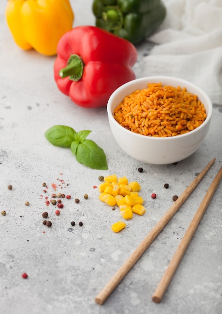 Prato de cerâmica branca com arroz basmati de grão longo vermelho cozido com legumes em fundo claro com palitos e pimenta páprica com milho, alho e manjericão.