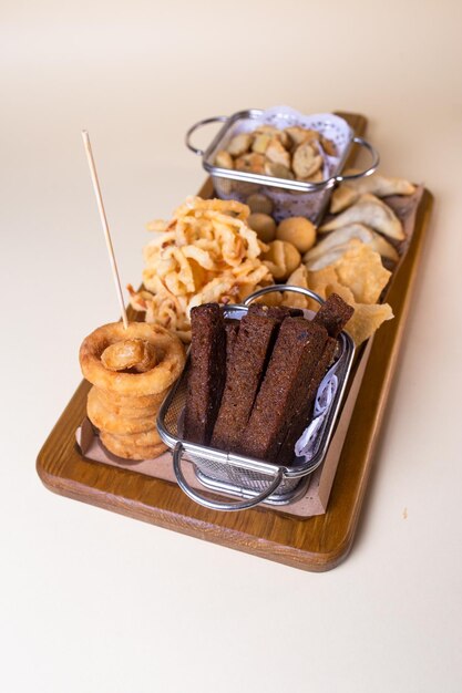 Foto prato de cerveja com croutons, anéis de cebola e batatas fritas em uma tábua de madeira