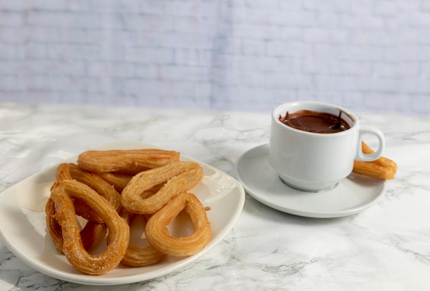 Prato de churros com açúcar e xícara de chocolate quente sobre fundo de mármore, típico espanhol