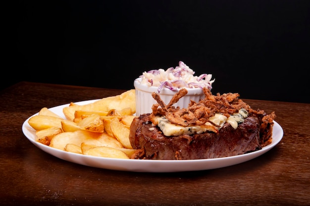 Prato de comida com bife suculento com queijo azul cebola crocante e batatas rústicas na madeira