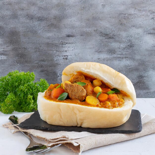 Foto prato de fast food sul-africano bunny chow curry com carne e vegetais em pão branco sobre um fundo branco