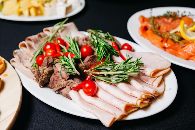 Prato de fatias finas de presunto e rosbife com pimenta vermelha e tomate cereja e alecrim