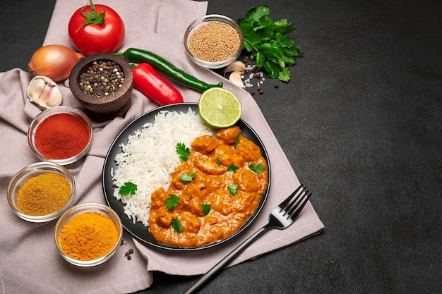 Prato de frango com curry tradicional, arroz e especiarias na mesa escura