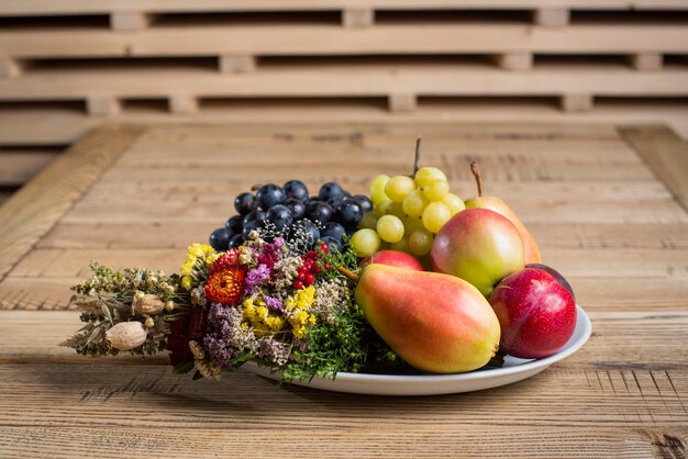 Prato de frutas com decorações de flores silvestres na mesa de madeira