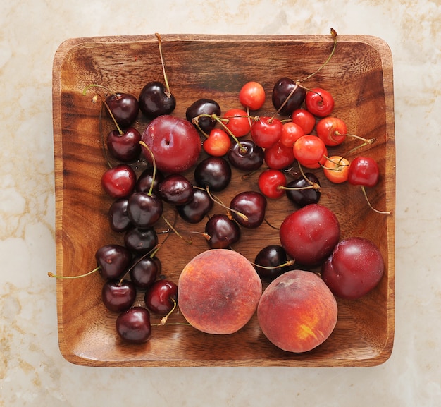 Prato de frutas - pêssegos, ameixas, cerejas no prato de madeira.