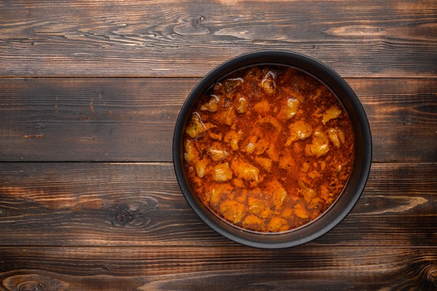 Prato de goulash húngaro tradicional caseiro em uma panela contra um fundo de madeira.