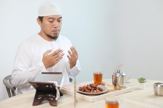 Prato de Iftar com homem muçulmano com a mão rezando a Alá Dates frutas com um copo de chá quente na mesa