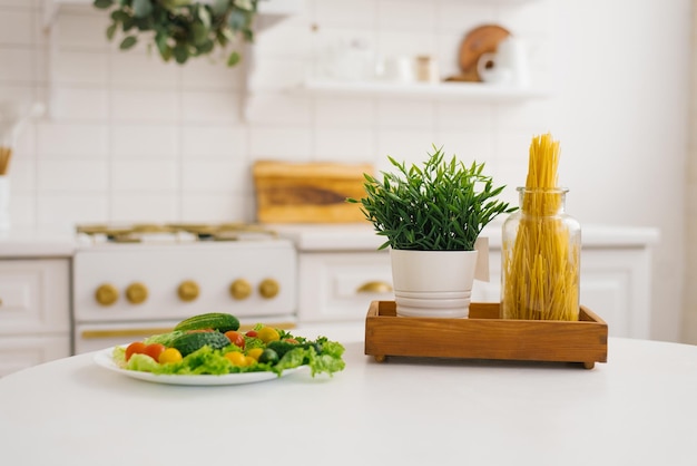 Prato de legumes, um pote de macarrão e uma planta verde na mesa da cozinha