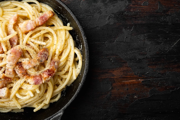 Prato de massa Carbonara. Cozinha tradicional romana. Conjunto de comida italiana, em frigideira de ferro fundido, na velha mesa de madeira escura, vista de cima plana, com espaço de cópia para o texto