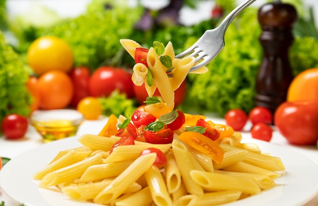 Prato de massa italiana cozida, penne rigate no garfo com tomate e folhas de manjericão