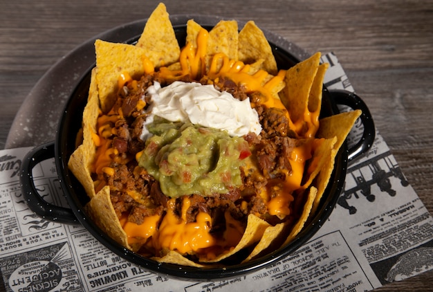 Prato de nachos com pimentão, creme de leite guacamole e molho cheddar na mesa de madeira. imagem isolada