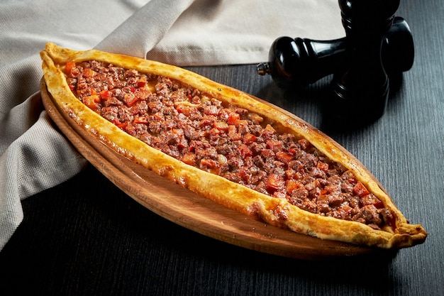 Prato de pide turco com fatias de carne, tomate na mesa preta