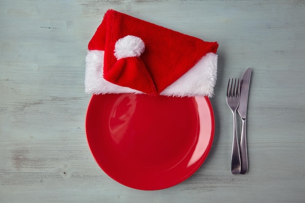 Prato de prato vermelho vazio com um boné de Natal e talheres em uma mesa de madeira azul