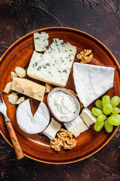 Prato de queijo com Brie, Camembert, Roquefort, Requeijão Azul, Uva e Nozes. Fundo escuro. Vista do topo.