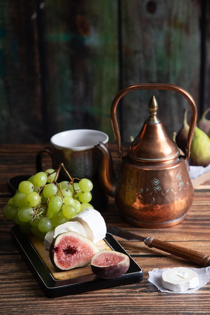 Prato de queijo com queijo de cabra, uvas e figos, vidro de ângulo de chaleira de cobre