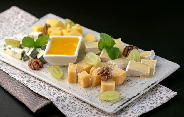 Prato de queijo com uvas de mel e nozes na mesa preta
