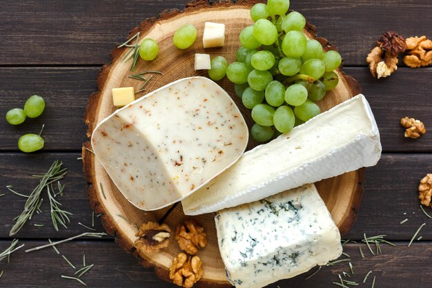 Prato de queijo, erva gouda e queijo roquefort azul na placa de madeira com uvas e nozes, natureza morta. vista do topo