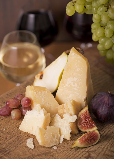 Prato de queijo servido com uvas melão figos biscoitos nozes e vinho branco em uma mesa de madeira