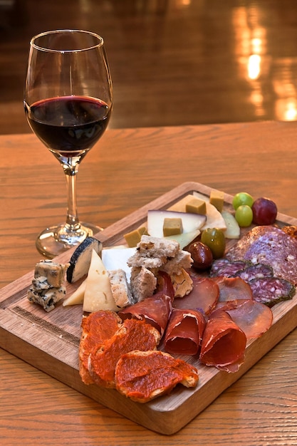 Prato de queijos e carnes frias acompanhado por um copo de vinho tinto em uma mesa de madeira em um restaurante