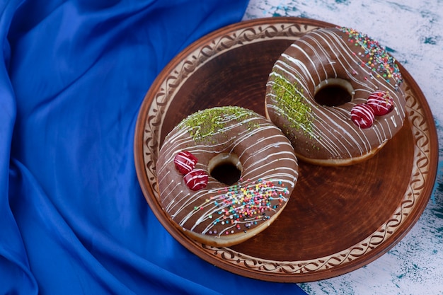 Prato de saborosos donuts de chocolate com granulado na superfície branca.