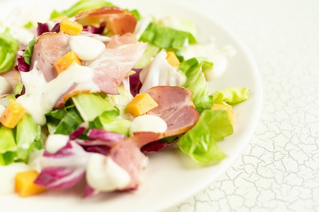 Prato de salada com folhas verdes, presunto, queijo e molho branco