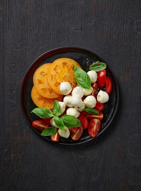 Prato de salada de tomate e mussarela na mesa da cozinha de madeira preta, vista superior