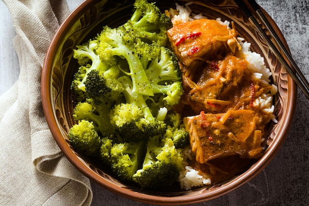 Prato de salmão tailandês em molho de coco com brócolis fresco e arroz em uma tigela de barro com pauzinhos alimentos saudáveis com vitamina B5