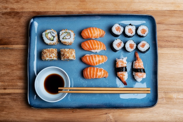 prato de sushi com Maki, Uramaki, Nigiri e California Roll num prato azul, soja e pauzinhos. Composição de alimentos gastronômicos asiáticos em fundo de madeira.