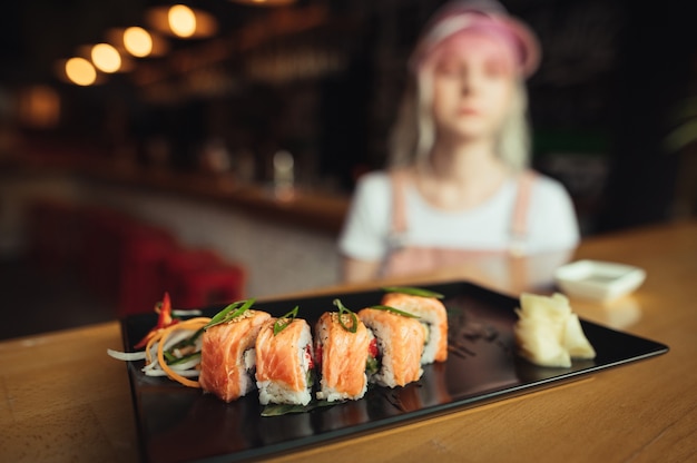 Foto prato de sushi rola em restaurante com uma mulher segurando os pauzinhos