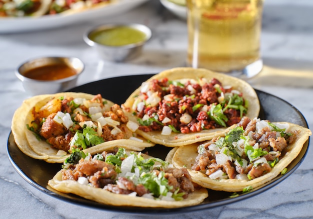 Foto prato de tacos de rua mexicanos com carne assada, chorizo e al pastor em tortilhas de milho