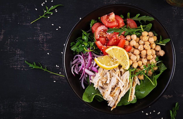 Prato de tigela de Buda com filé de frango, grão de bico, tomate, cebola roxa, salada verde fresca e gergelim de semente. Uma alimentação saudável e equilibrada. Vista superior, acima, copie o espaço