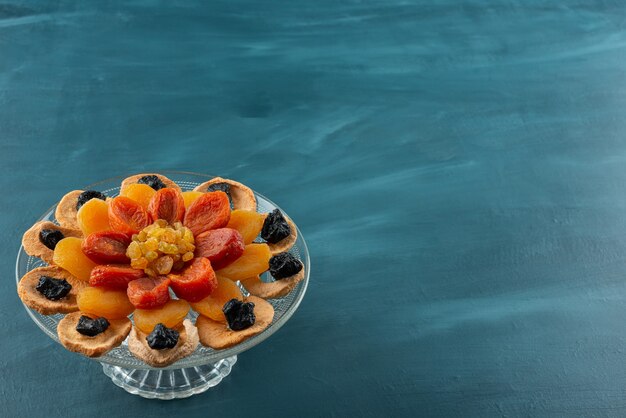 Prato de vidro com várias frutas secas colocadas na mesa azul.