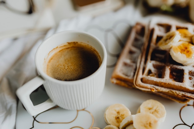 Prato de waffle com fatias de banana e uma xícara de café