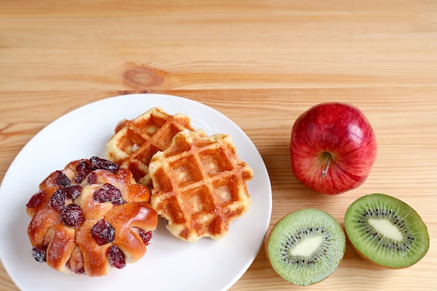 Prato de waffles belgas e pão de passas na mesa de madeira com maçã e kiwi cortado com espaço de cópia