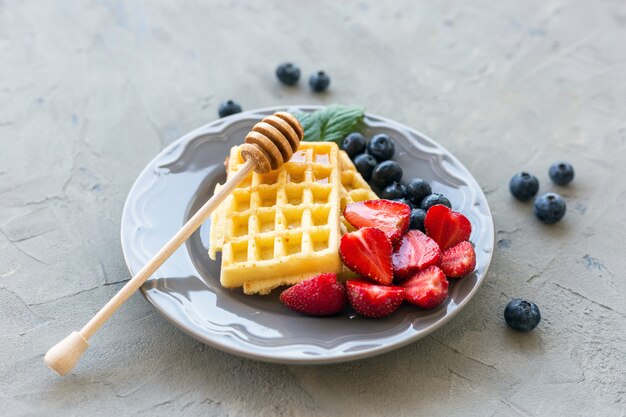 Prato de waffles decorado com mel e frutas frescas na superfície de pedra cinza. conceito de comida. vista do topo.