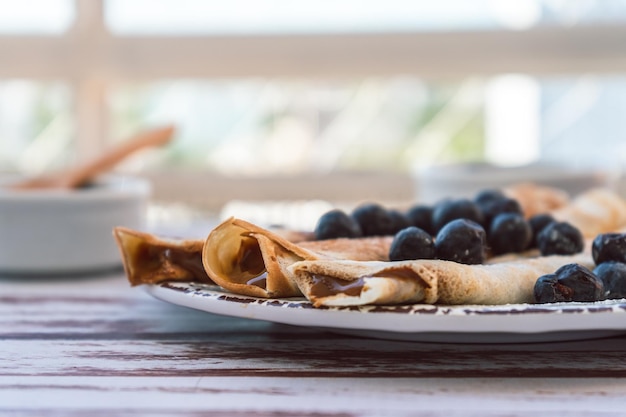 Prato delicioso com panquecas ou crepes caseiros recheados com doce de leite e mirtilos e açúcar de confeiteiro cobrindo o prato