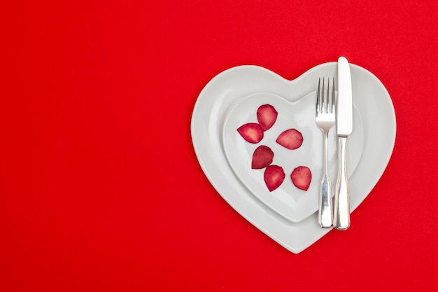 Prato em forma de coração com faca e garfo em um fundo vermelho