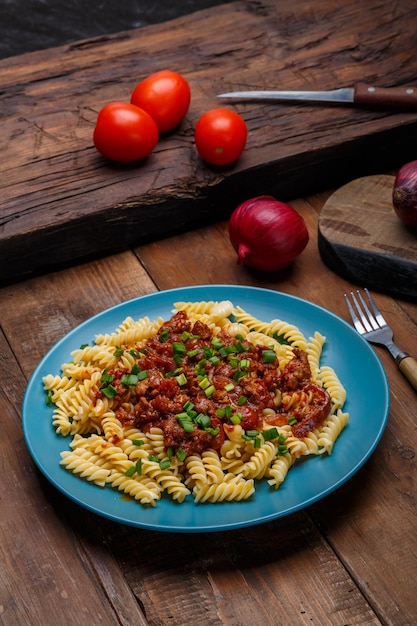 Prato grande com macarrão à bolonhesa em uma mesa de madeira ao lado de tomate