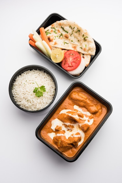 Prato indiano com manteiga e frango com curry servido em recipiente de plástico preto para entrega em casa