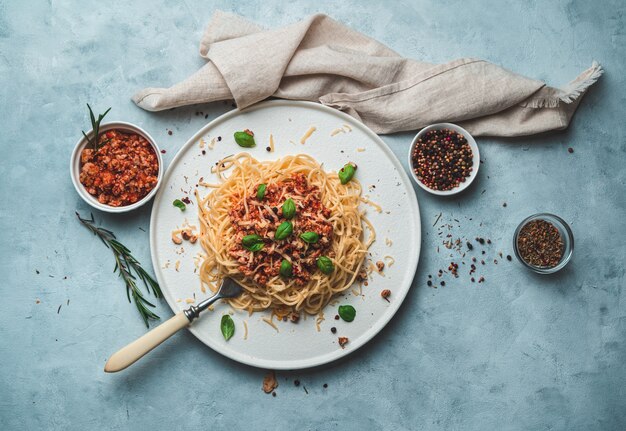 Prato italiano à bolonhesa em um prato raso branco com temperos e um guardanapo bege em um cinza-azulado