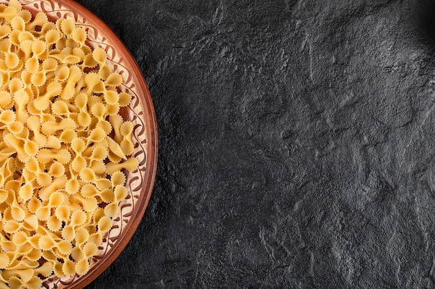 Prato marrom de macarrão cru colocado na mesa preta.