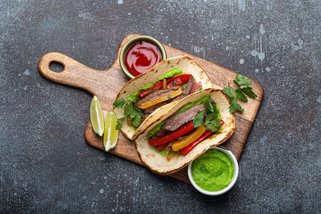 Prato mexicano tradicional Tacos de fajitas de carne servidos em uma tábua de madeira com molho de tomate e guacamole em um fundo de pedra rústico de cima, comida mexicana americana