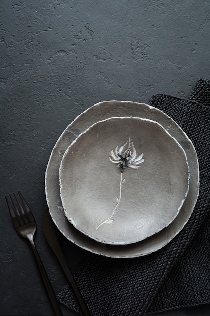 Prato plano vazio-rústico de argila cinza com uma bela flor na mesa de concreto preta. Foco seletivo. Vista do topo. Copie o espaço.