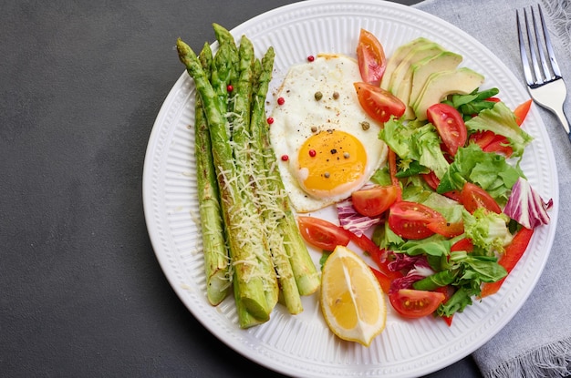 Prato redondo com espargos cozidos, ovo frito, abacate e salada de legumes frescos na mesa