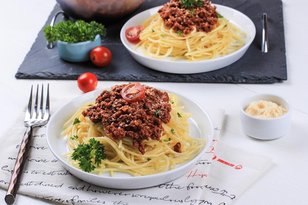 Prato saudável de espaguete italiano coberto com um saboroso molho à bolonhesa de tomate e carne moída e salsa fresca em uma mesa de madeira branca