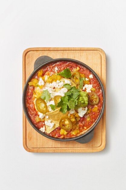 Prato tradicional do Oriente Médio Shakshuka de ovos fritos com tomate, pimentão, legumes e ervas em uma panela em uma placa de madeira sobre um fundo cinza claro, copie o espaço. Vista do topo.