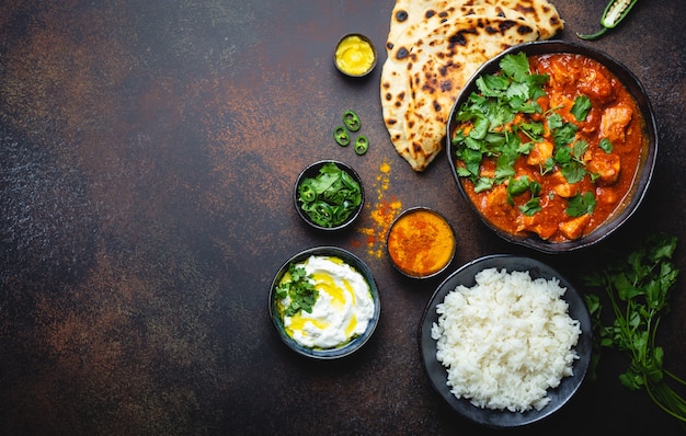 Prato tradicional indiano Frango tikka masala com espaço para texto. Carne picante de curry na tigela, arroz basmati, pão naan, molho raita de iogurte em fundo escuro rústico, vista de cima, close-up, espaço de cópia