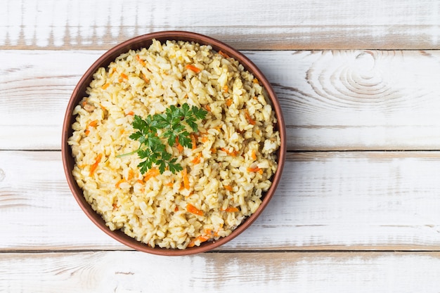 Prato vegetariano ensopado de arroz integral com cebola e cenoura em uma tigela em uma luz de madeira
