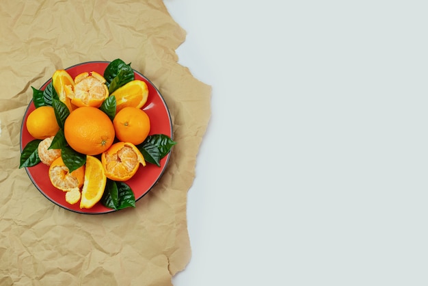 Prato vermelho de laranjas e tangerinas com folhas verdes sobre um fundo claro